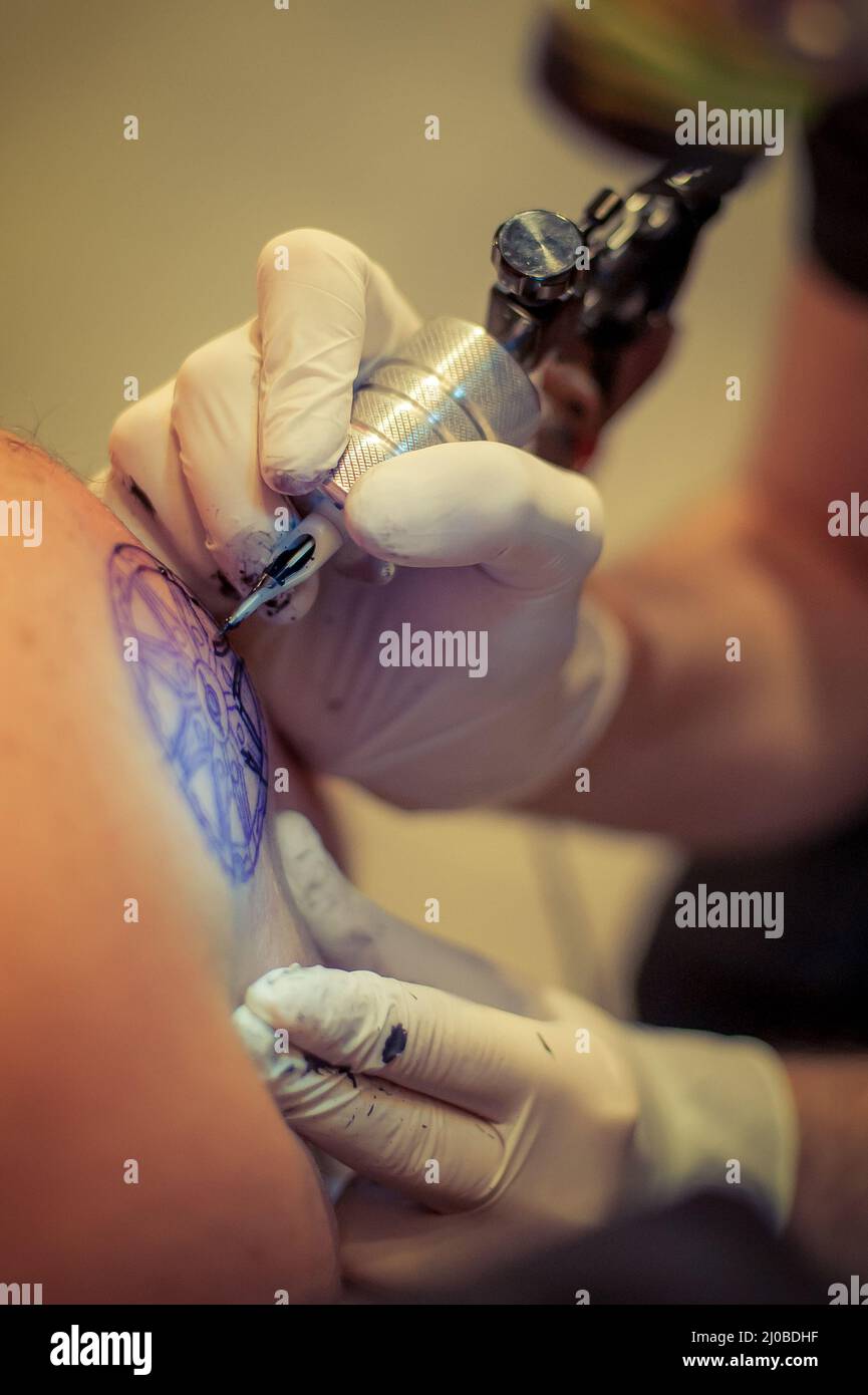 Le tatouage maître dessine la peinture bleue sur le tatouage client Banque D'Images