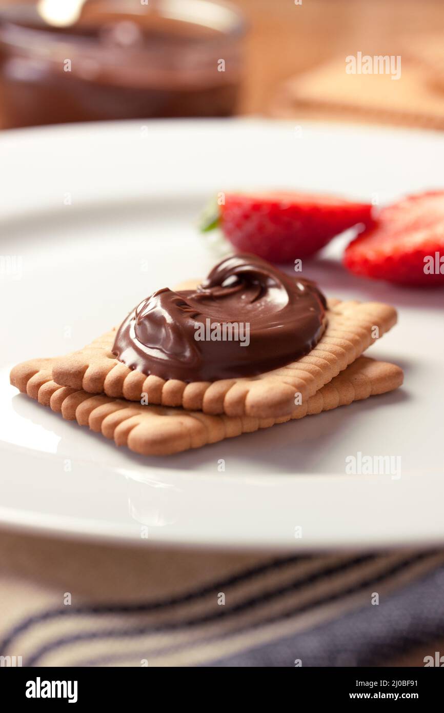 Crème de nougat douce au chocolat sur des biscuits et des fraises sur une assiette blanche. Banque D'Images