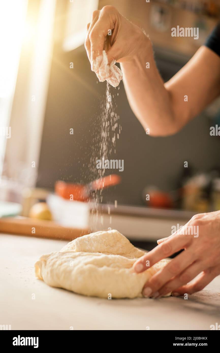 Les mains de la femme pétrir de la pâte sur la table dans sa cuisine. Gros plan Banque D'Images