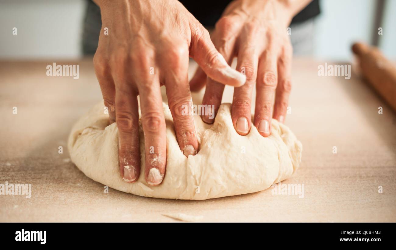 Les mains de la femme pétrir de la pâte sur la table dans sa cuisine. Gros plan Banque D'Images