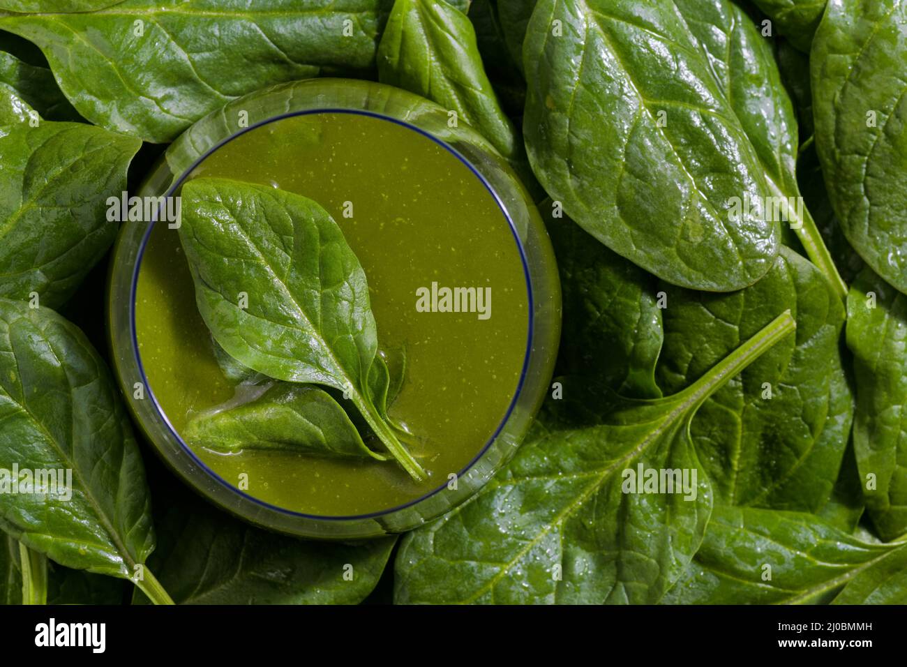 Vue de dessus d'un bol en verre rempli d'un smoothie aux légumes d'épinards entouré de feuilles d'épinards crues. Banque D'Images
