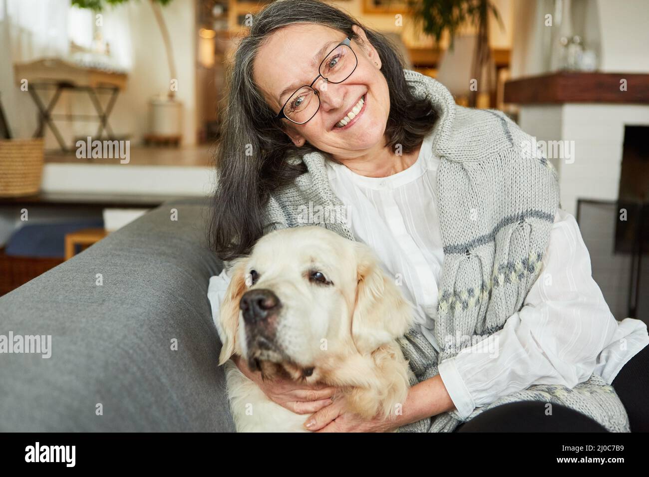 Une femme âgée en tant que pensionnée heureuse se câliner avec son chien retriever sur le canapé à la maison Banque D'Images