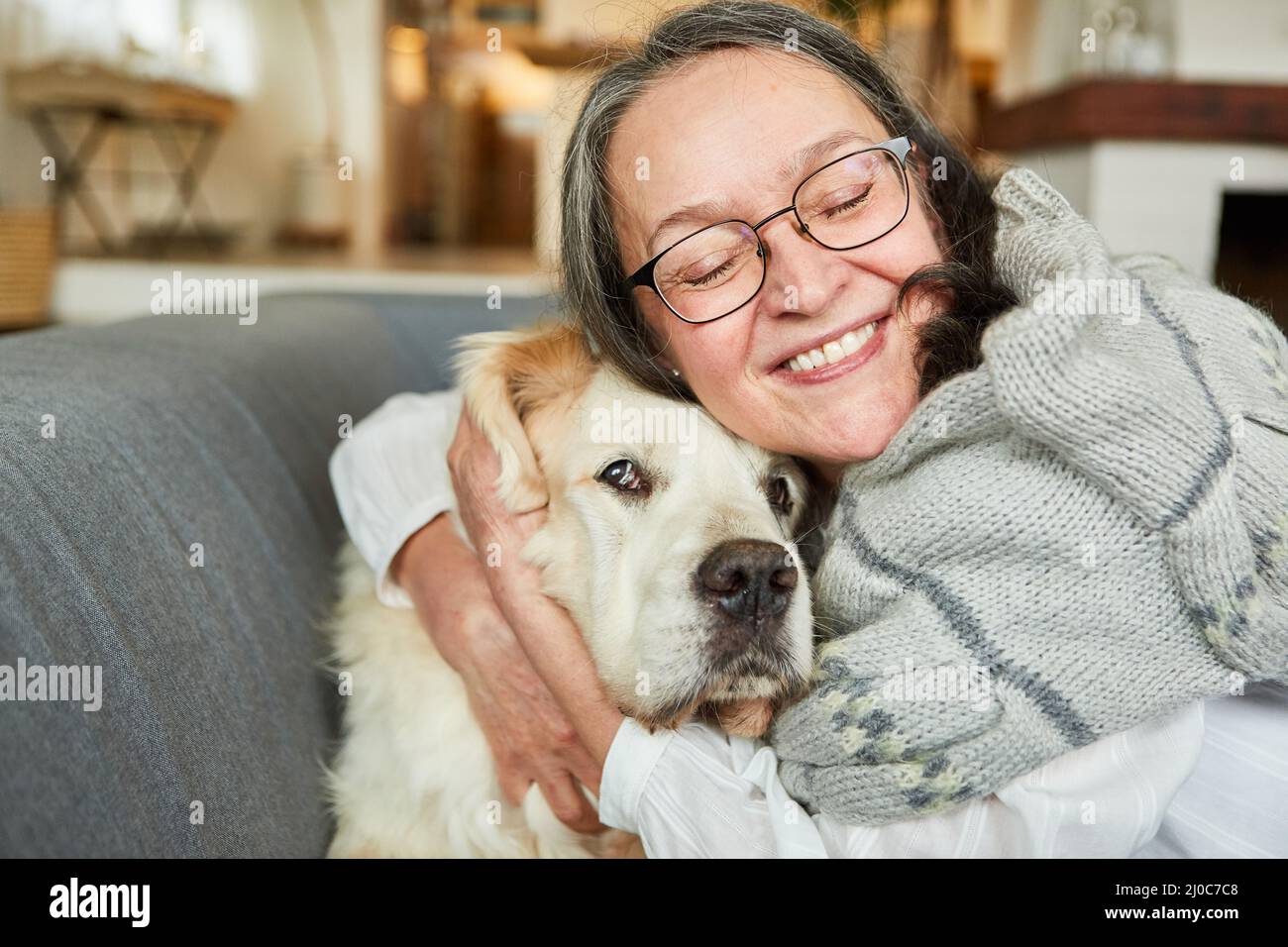 Une femme âgée tue son grand chien de retriever à la maison sur le canapé contre la solitude Banque D'Images