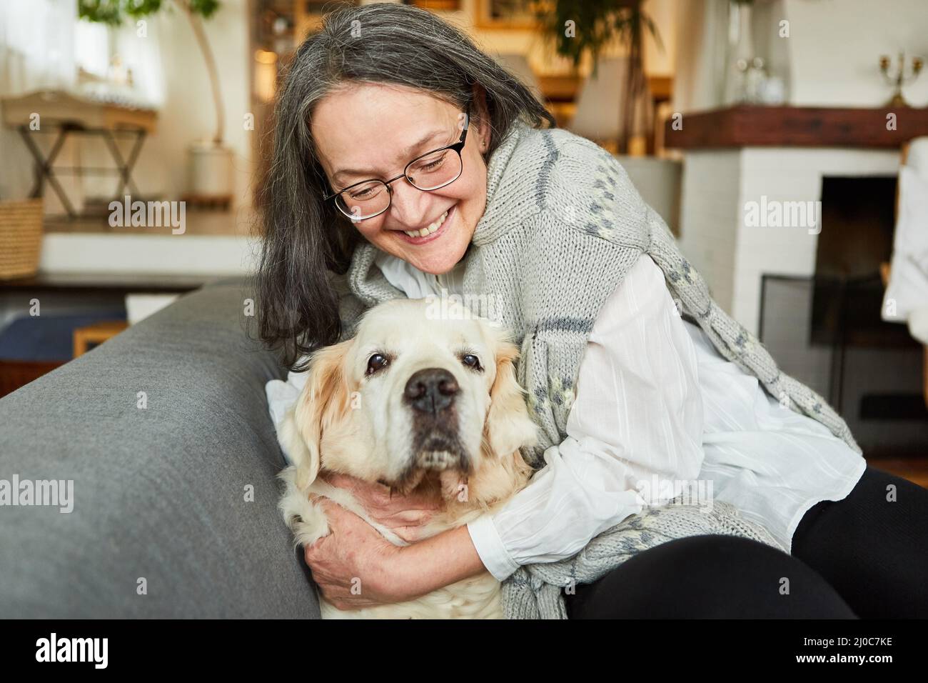 Bonne femme âgée à la retraite, qui se câlin avec son chien retriever sur le canapé à la maison Banque D'Images
