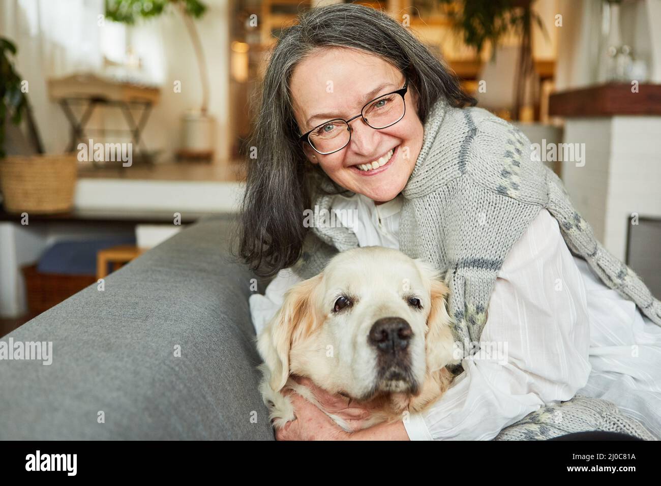 Une femme âgée en tant que pensionné heureux tue son grand chien à la maison sur le canapé pour l'amitié Banque D'Images