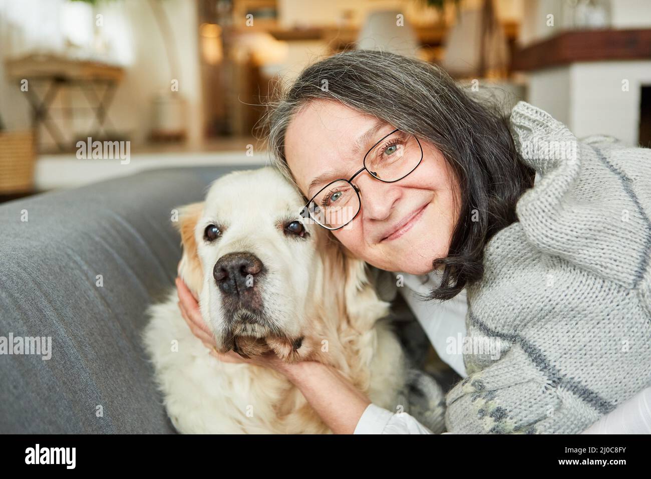 Une femme âgée se câlin avec son chien de retriever sur le canapé à la maison pour l'amour des animaux et l'amitié Banque D'Images