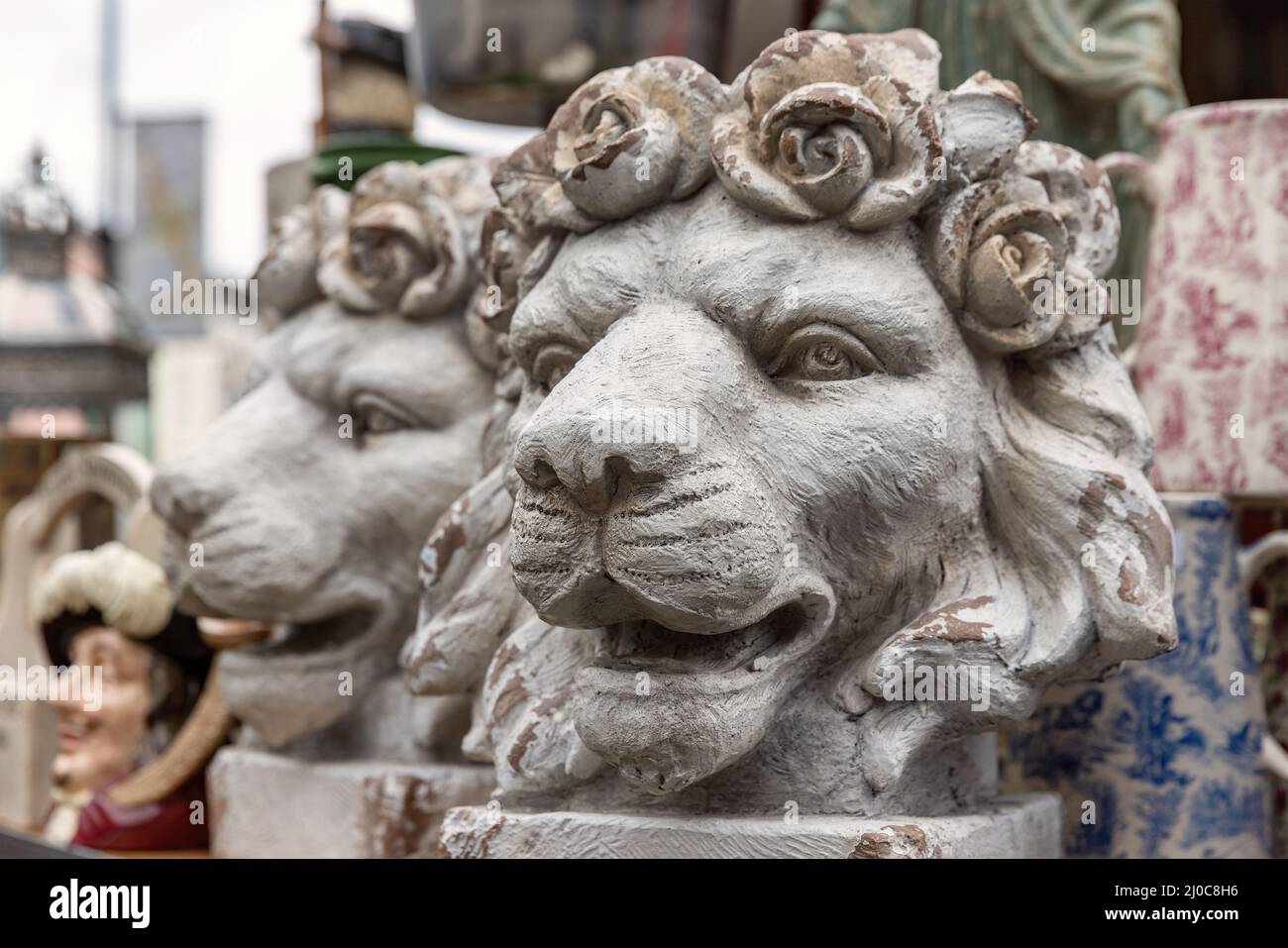 Une paire de pots décoratifs antiques de plantes à tête de lion, avec des roses formant la manie. D'autres antiquités et bric-a-brac peuvent être vus dans le fond d'une marque Banque D'Images