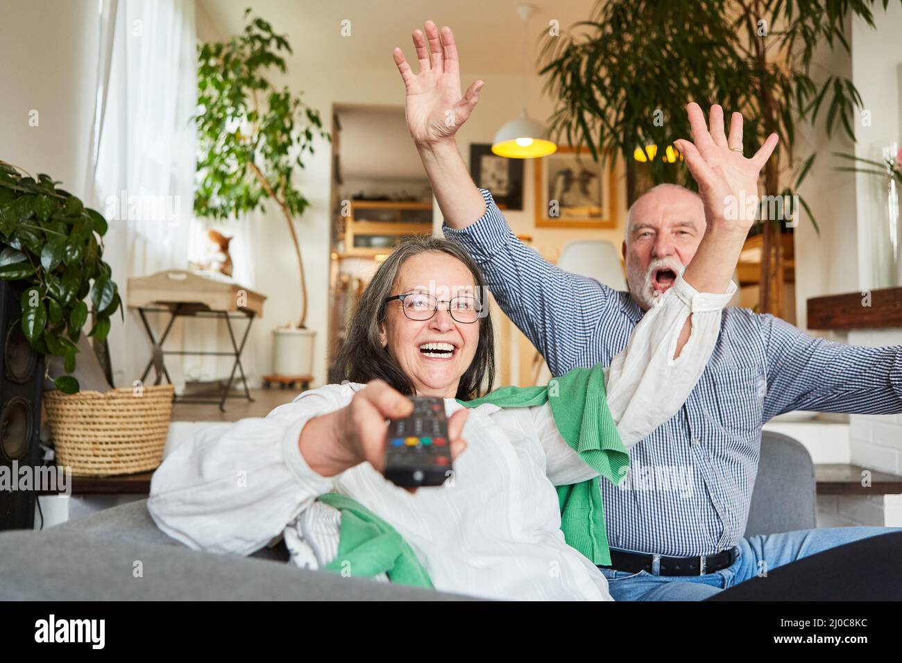 Encourager un couple d'aînés avec télécommande de télévision est heureux de gagner la loterie à la maison dans le salon Banque D'Images