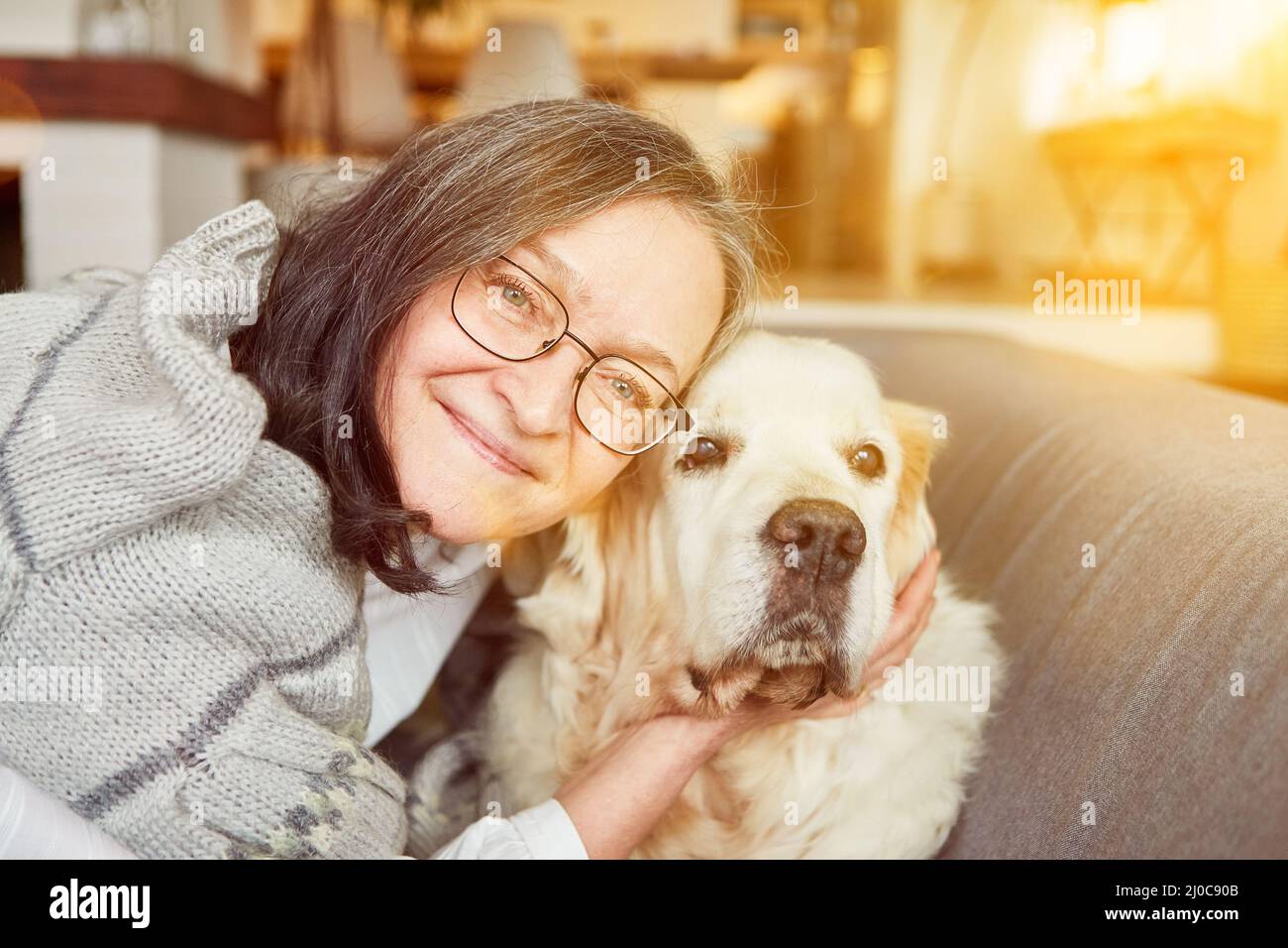 Vieille femme en tant que femme âgée qui se batte et se câlin avec un chien comme animal de compagnie à la maison dans la salle de séjour Banque D'Images