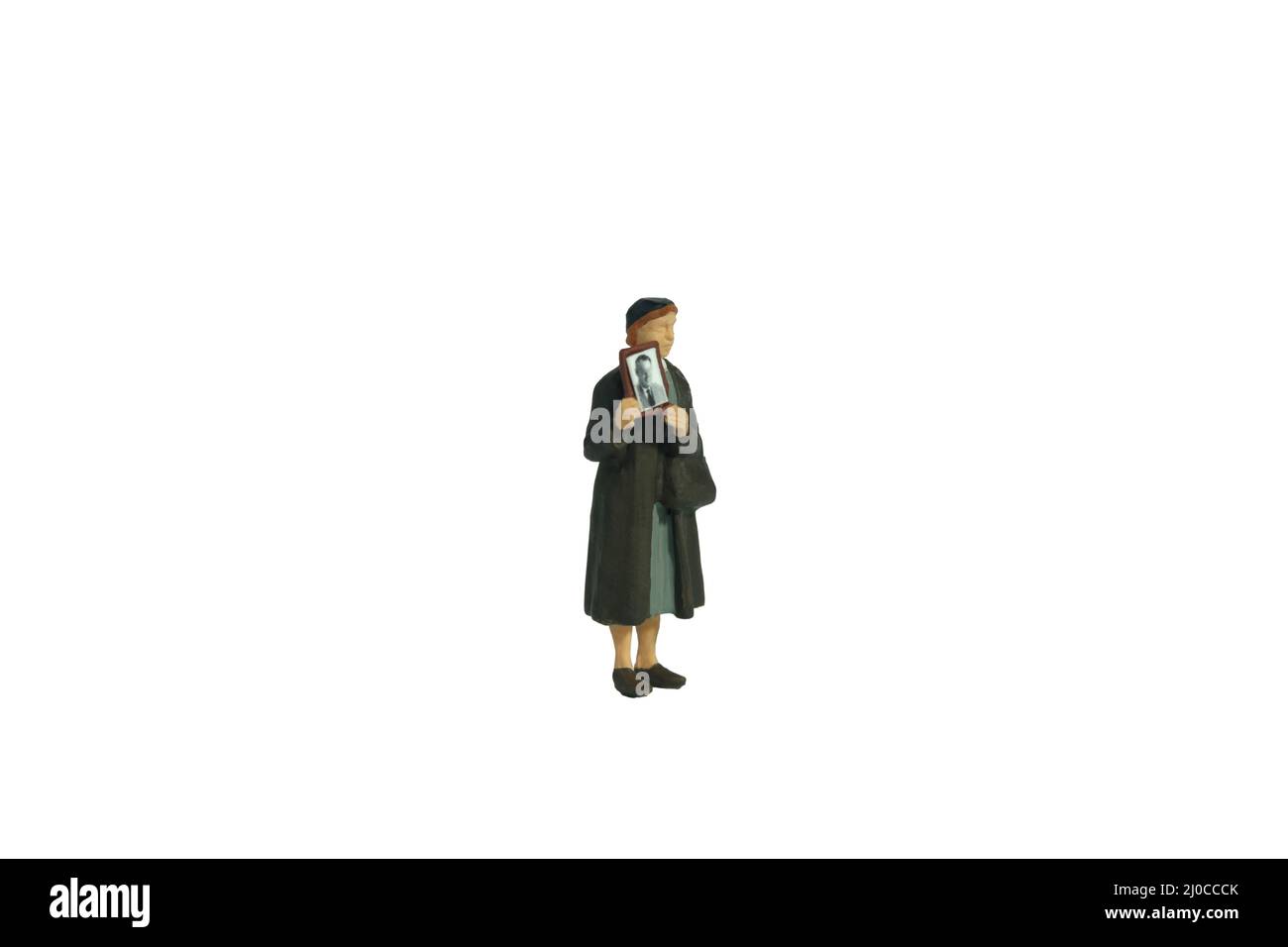 Photographie miniature de personnage de jouet de personnes. Une femme tenant un cadre photo, recherchant une personne manquante en raison d'un conflit de guerre. Isolé sur fond blanc. Banque D'Images