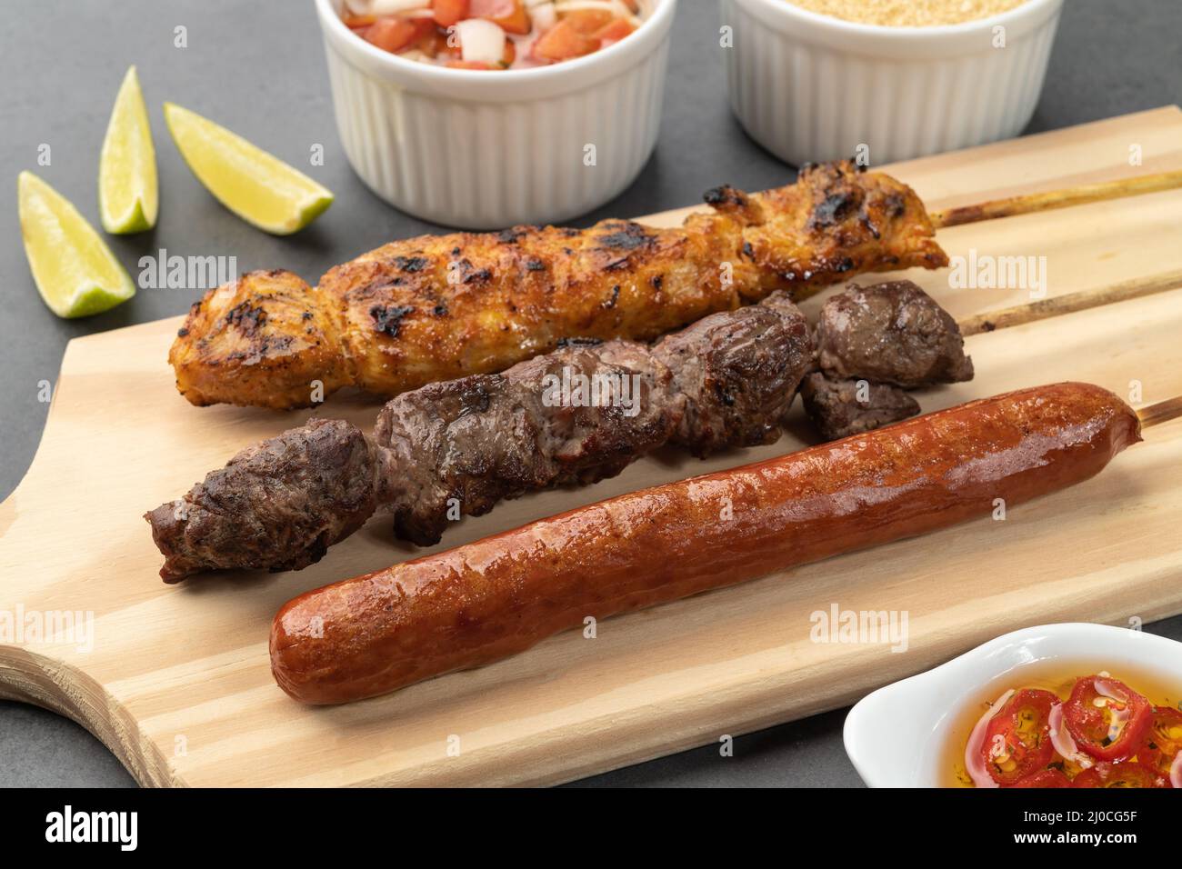 Brochettes de viande, poulet et saucisse de porc sur une planche de bois avec farofa et vinaigrette. Banque D'Images