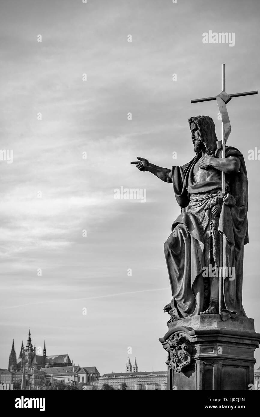 Statue de Jean-Baptiste sur le pont Charles et la ligne d'horizon de Prague, République tchèque. Paysage urbain noir et blanc. Sculpture : Josef Max, 1857 Banque D'Images