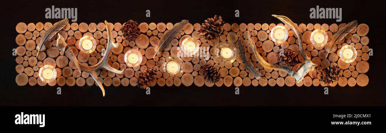 Décoration de table rustique, vue sur le dessus. Table longue avec thème nature ou chasse. Bougies allumées, bois de cerf, plumes et anneau en bois de cèdre ensemble o Banque D'Images