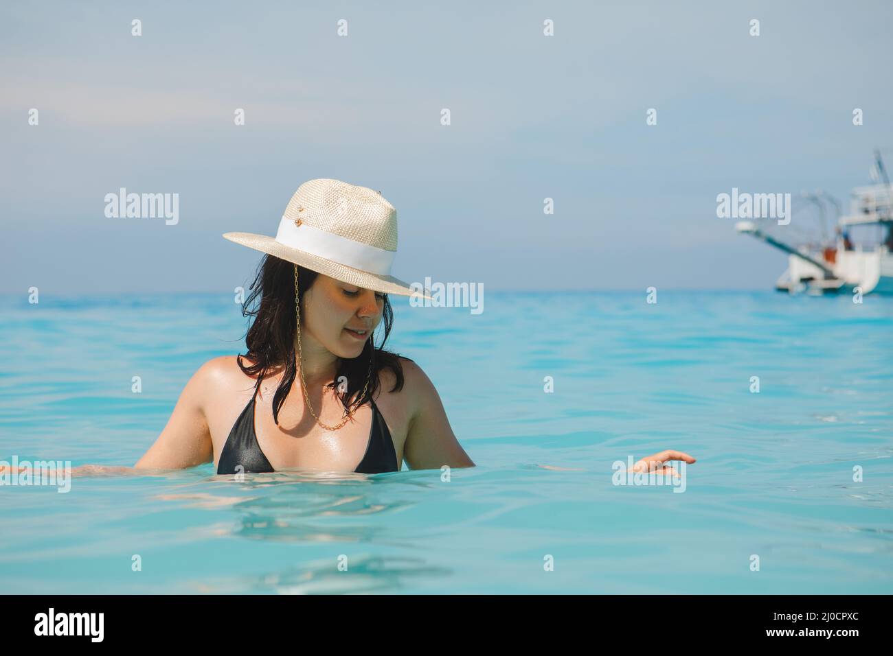 femme en chapeau blanc et maillot de bain noir en bleu eau de mer vacances d'été Banque D'Images