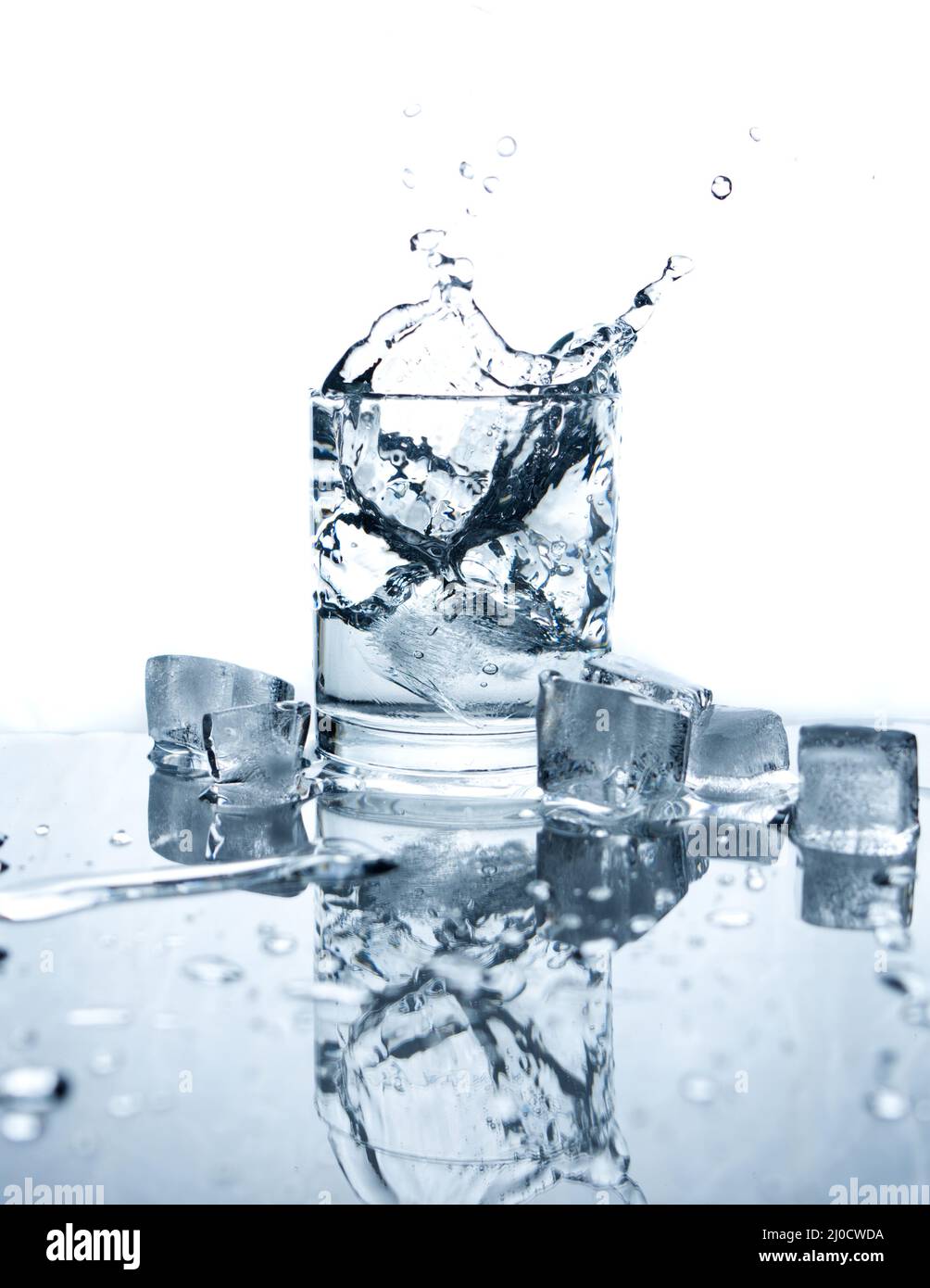 L'eau potable éclaboussé avec de la glace dans le verre sur fond blanc avec des reflets. Banque D'Images