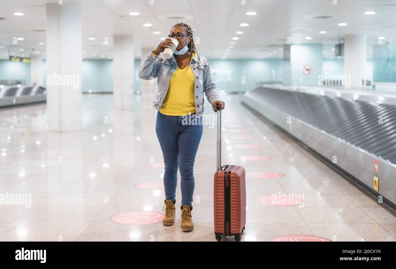 Femme africaine marchant dans le terminal de l'aéroport avec des bagages tout en buvant une tasse de café Banque D'Images