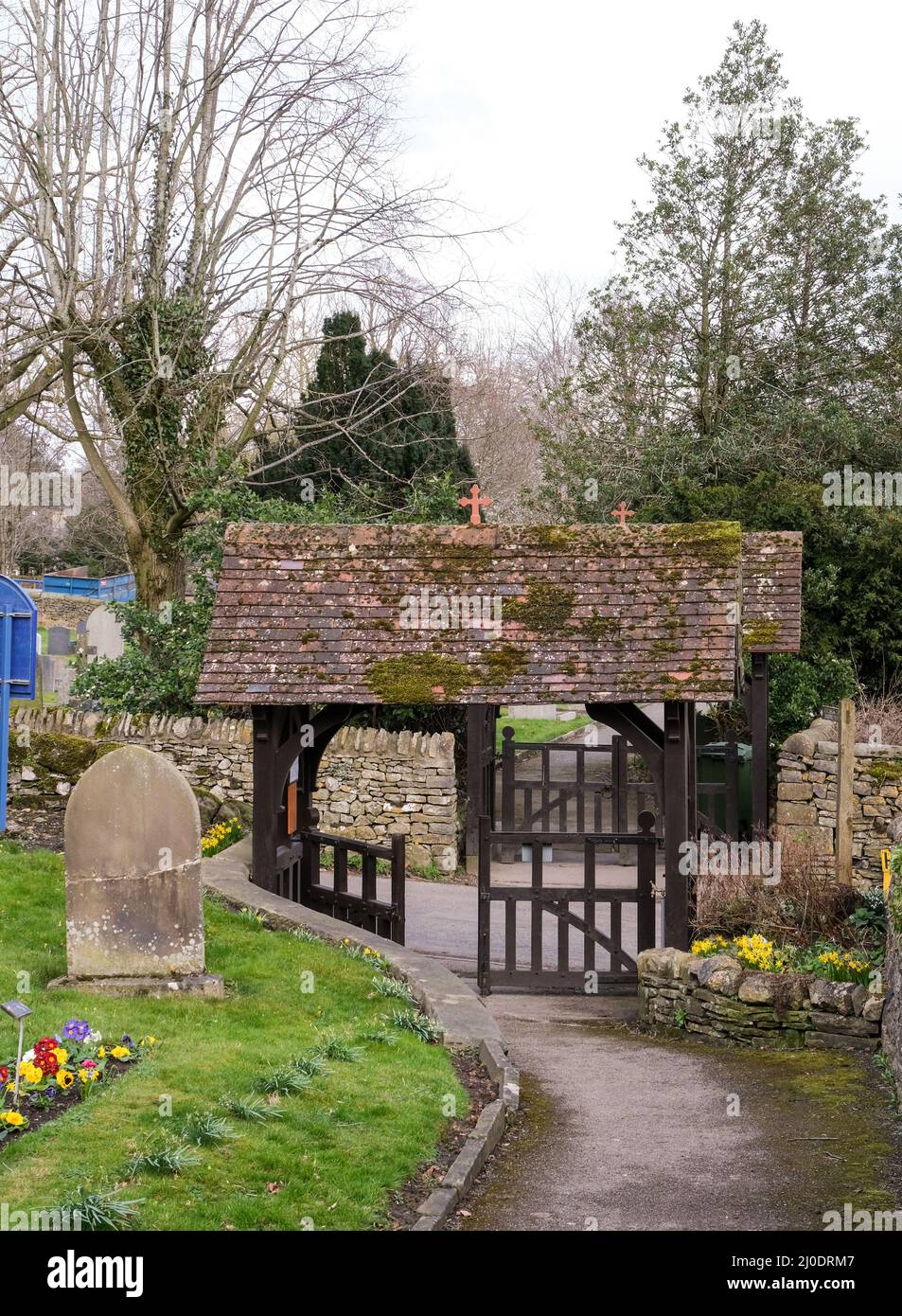 Une double porte lyque à l'extérieur de l'église de St Giles dans le village de Derbyshire de Great Longstone. Les toits de tuiles sont recouverts de mousse et de lits de fleurs li Banque D'Images