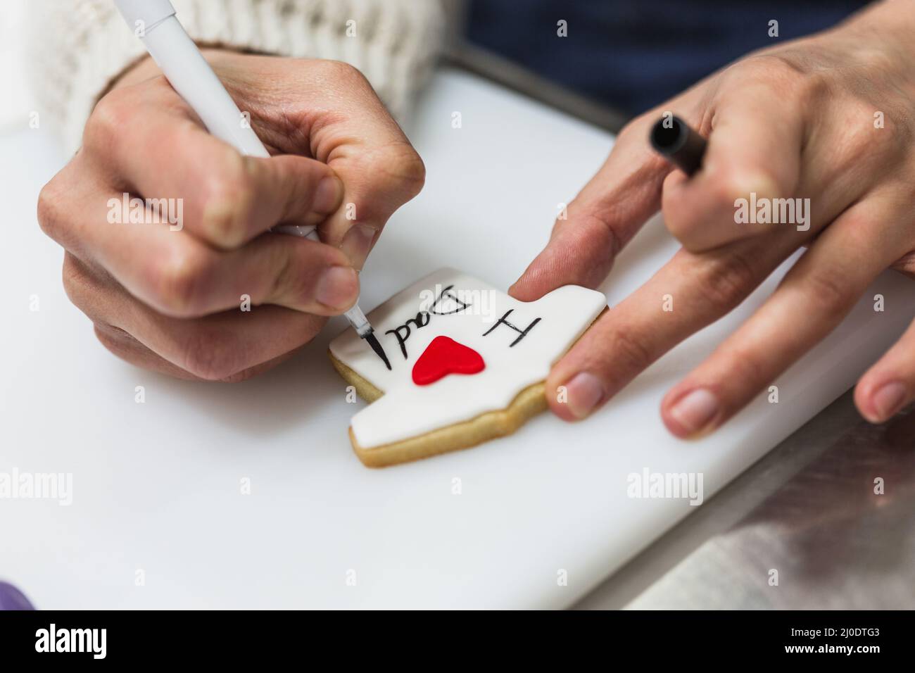 Vue rapprochée d'une femme chef pâtissier qui écrit et dessine à la main un cookie. Banque D'Images