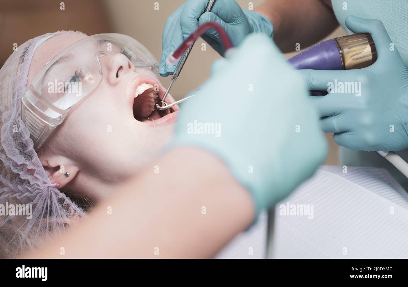 Belle fille en chaise dentaire à l'examen chez le dentiste. Femme montrant ses dents blanches droites parfaites. Outils de la technologie de la lampe à ultraviolet. Banque D'Images