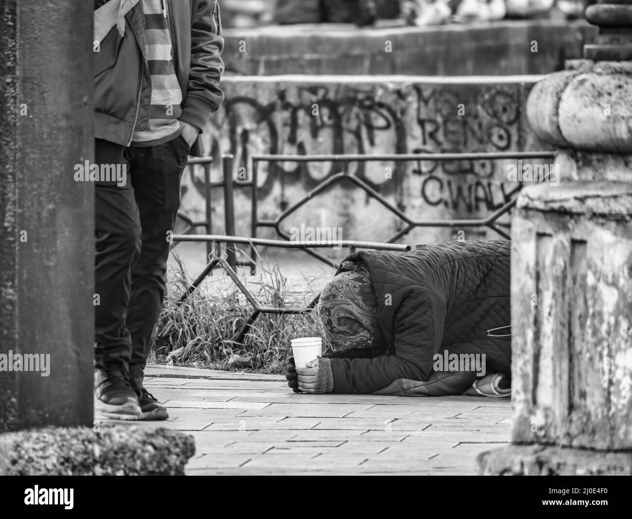 Vieille femme pauvre âgée avec son visage vers le bas sur la promenade latérale. Mendiant dans le centre de Bucarest, Roumanie Banque D'Images