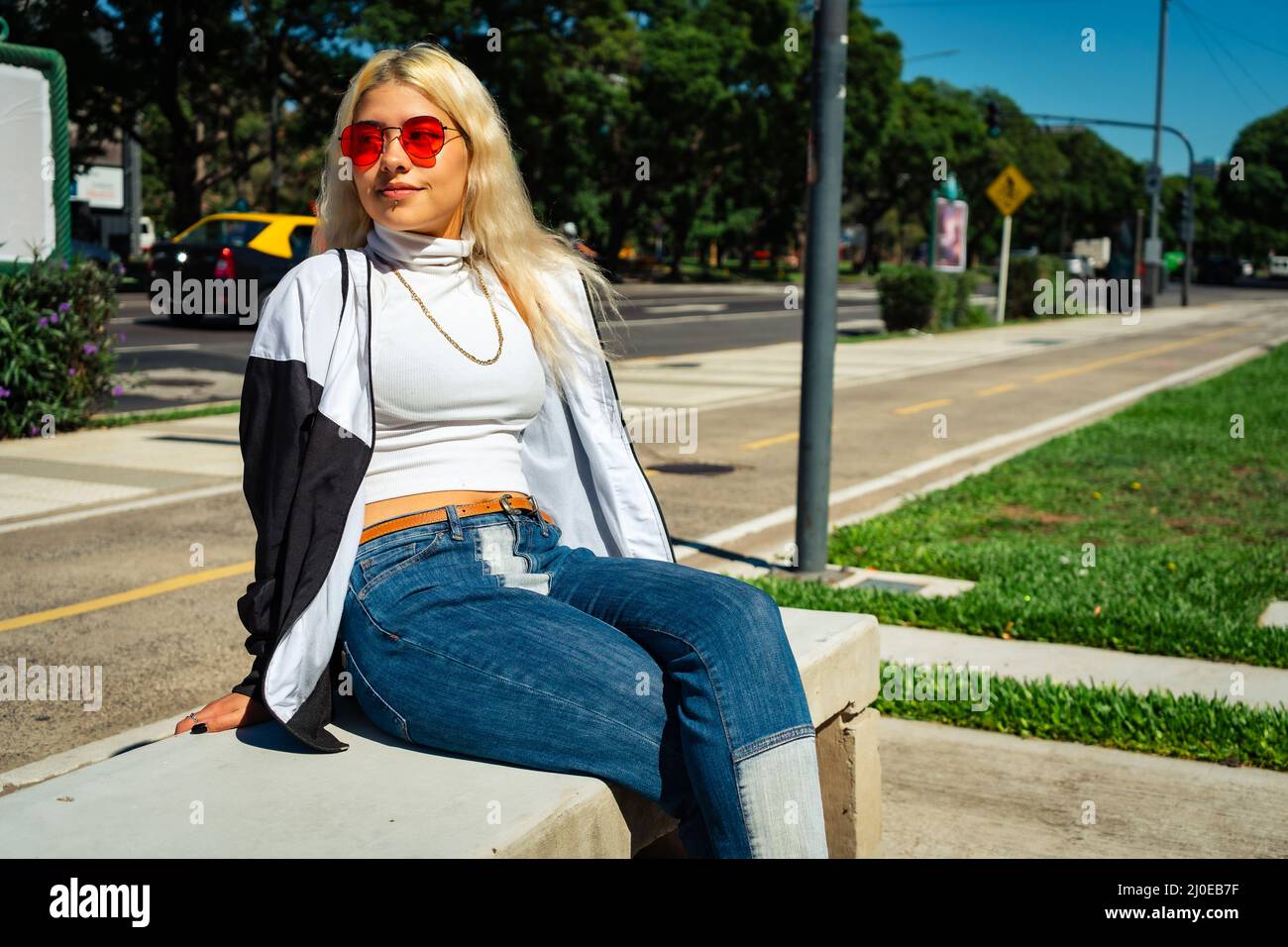 Belle jeune femme latine dans un t-shirt blanc assis sur un banc dans un parc public. Concept de femme moderne. Banque D'Images