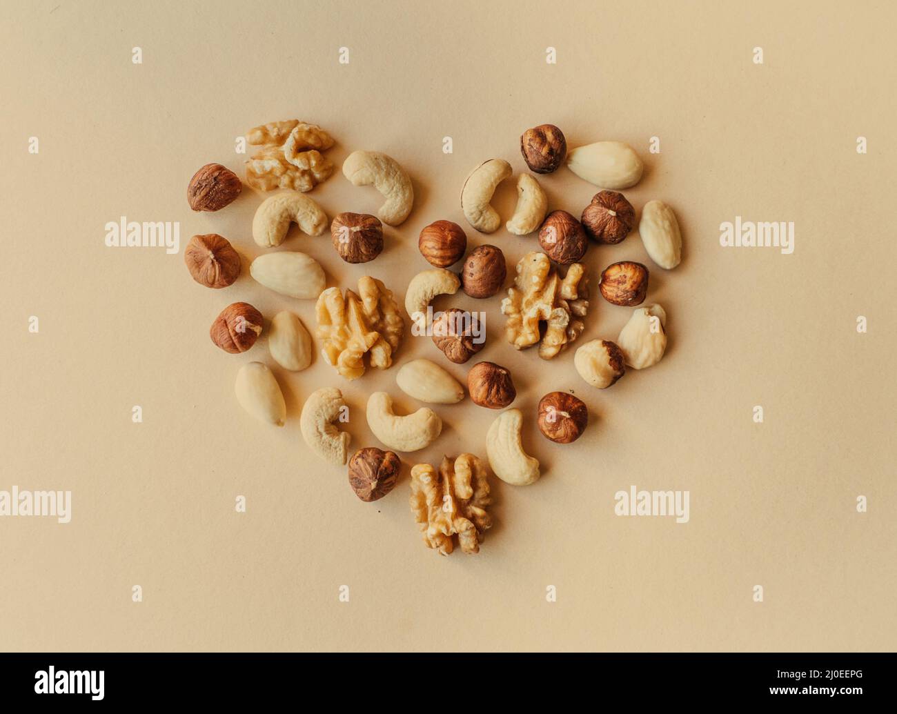 Une variété de noix, noix, amandes, noisettes et noix de cajou disposés de sorte que l'apparence d'un coeur isolé sur fond beige Banque D'Images