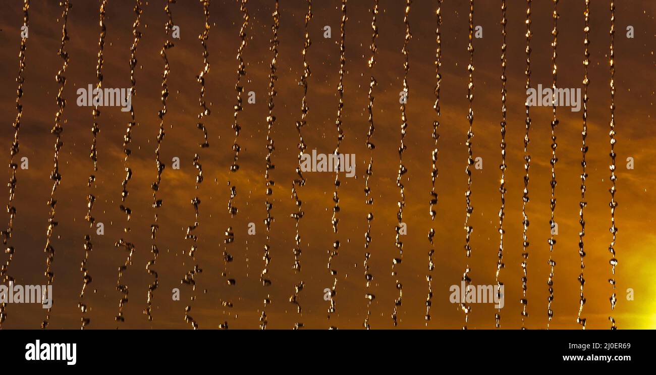 L'eau s'écoule d'un toit en lignes parallèles droites, mises en évidence par un soleil couchant et un beau coucher de soleil. Banque D'Images