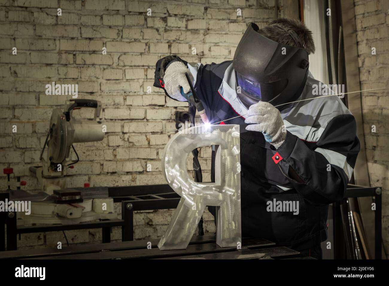 Soudeur soudant une pièce métallique dans un environnement industriel, portant un équipement de protection standard. Banque D'Images