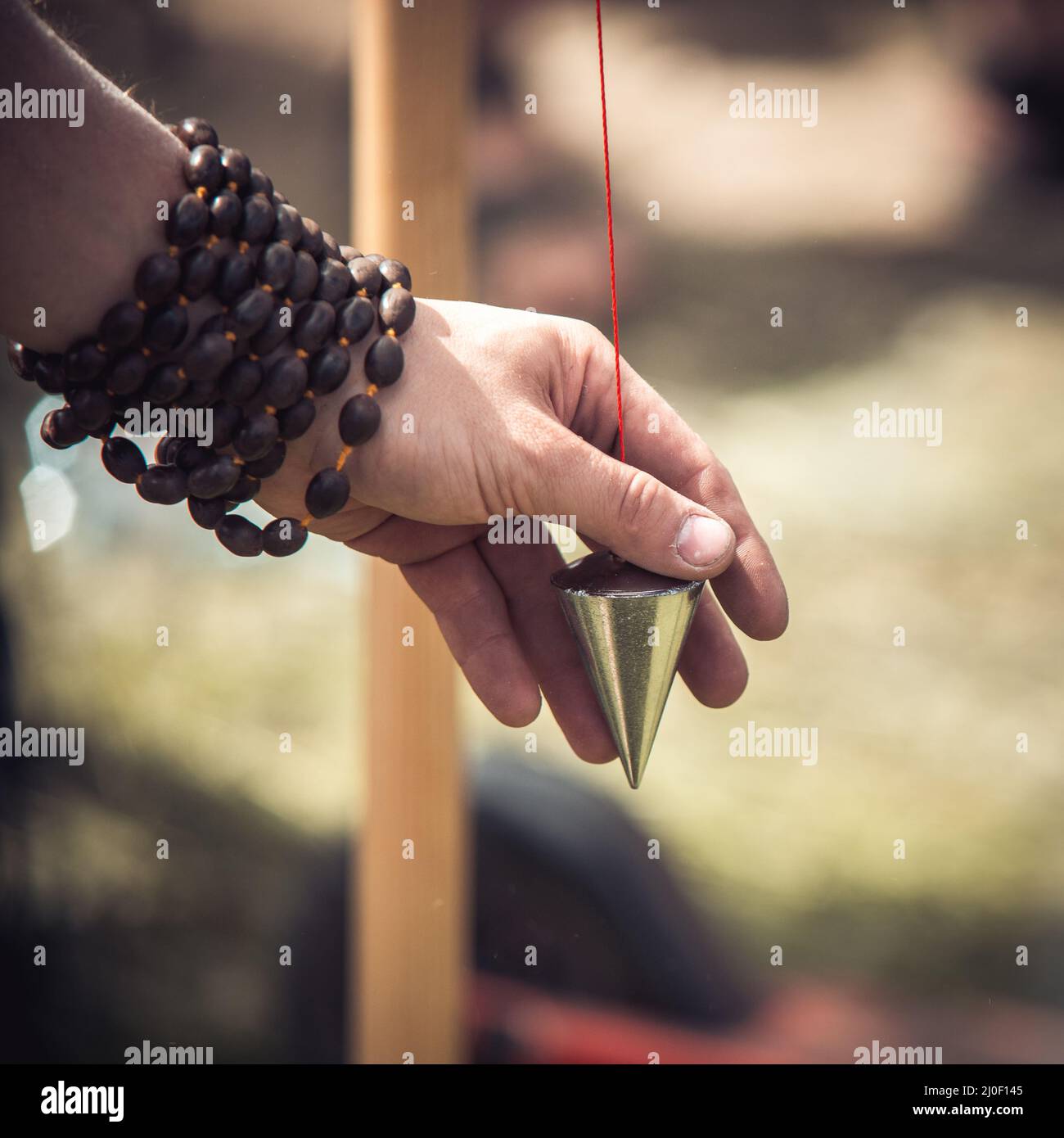 La main d'homme blanc caucasien mâle avec un bracelet en bois tient un fil à plomb conique ancien d'époque Banque D'Images