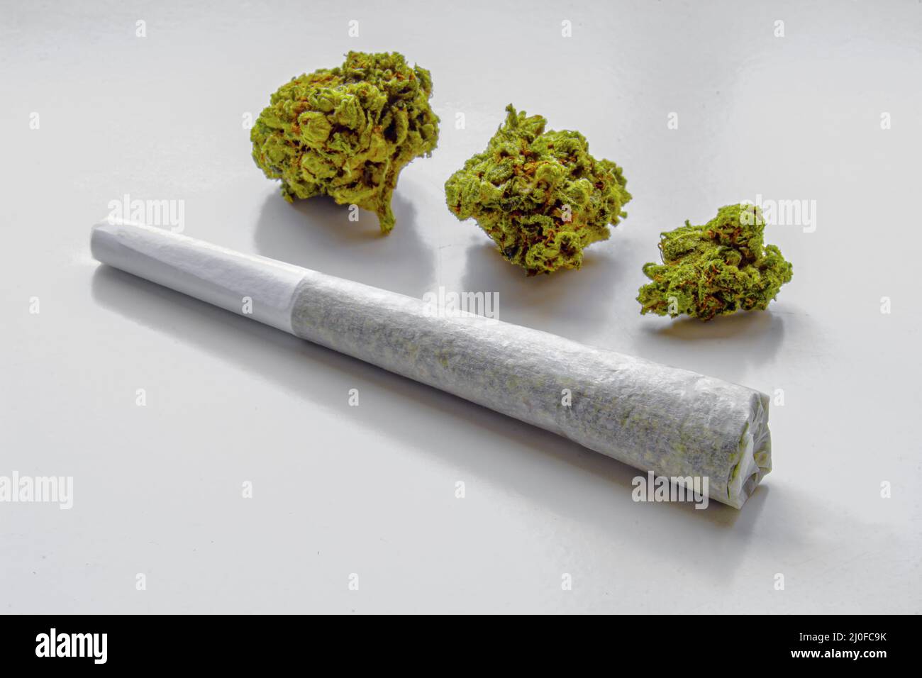 Un pré-rouleau de cannabis médicinal joint sur une surface blanche avec 3 fleurs de cannabis sur le fond Banque D'Images