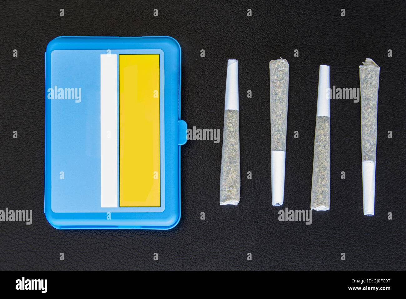 Quatre joints de Legal Canadian Cannabis sur fond de cuir noir. 2 grammes par joint et boîtier en plastique bleu. Banque D'Images