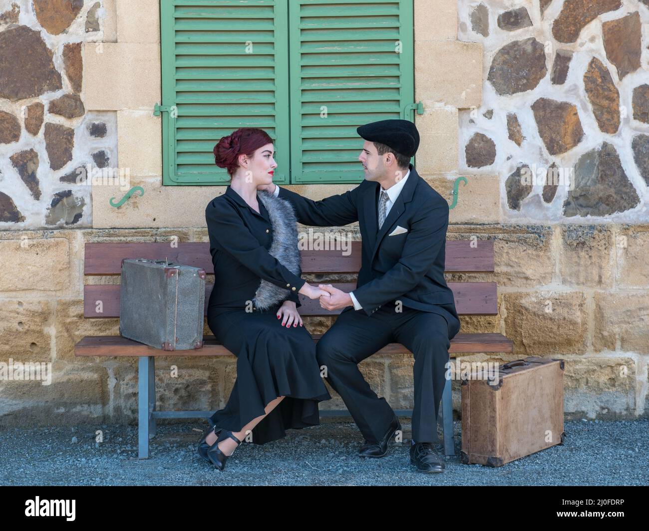 Jeune beau couple vêtu de vêtements vintage assis sur un banc et parlant Banque D'Images