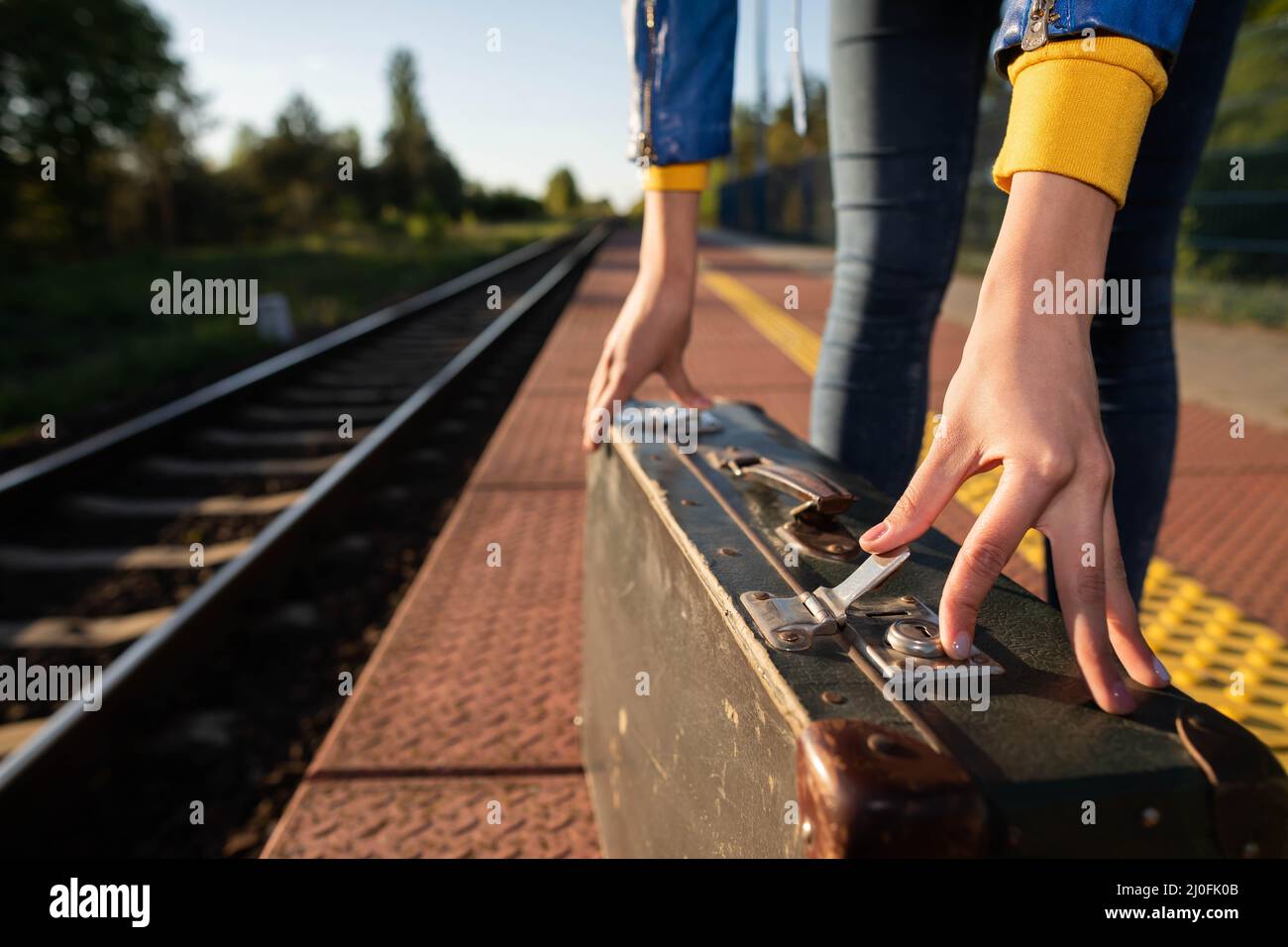 Une fille attache la fermeture éclair sur une vieille valise de voyage sur une plate-forme de train un après-midi d'été lors d'un voyage en train prévu. Banque D'Images