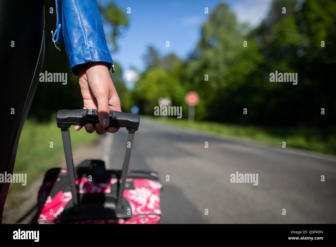Une jeune main femelle tient une poignée noire d'une valise rose sur roues et tout vu de près. Banque D'Images