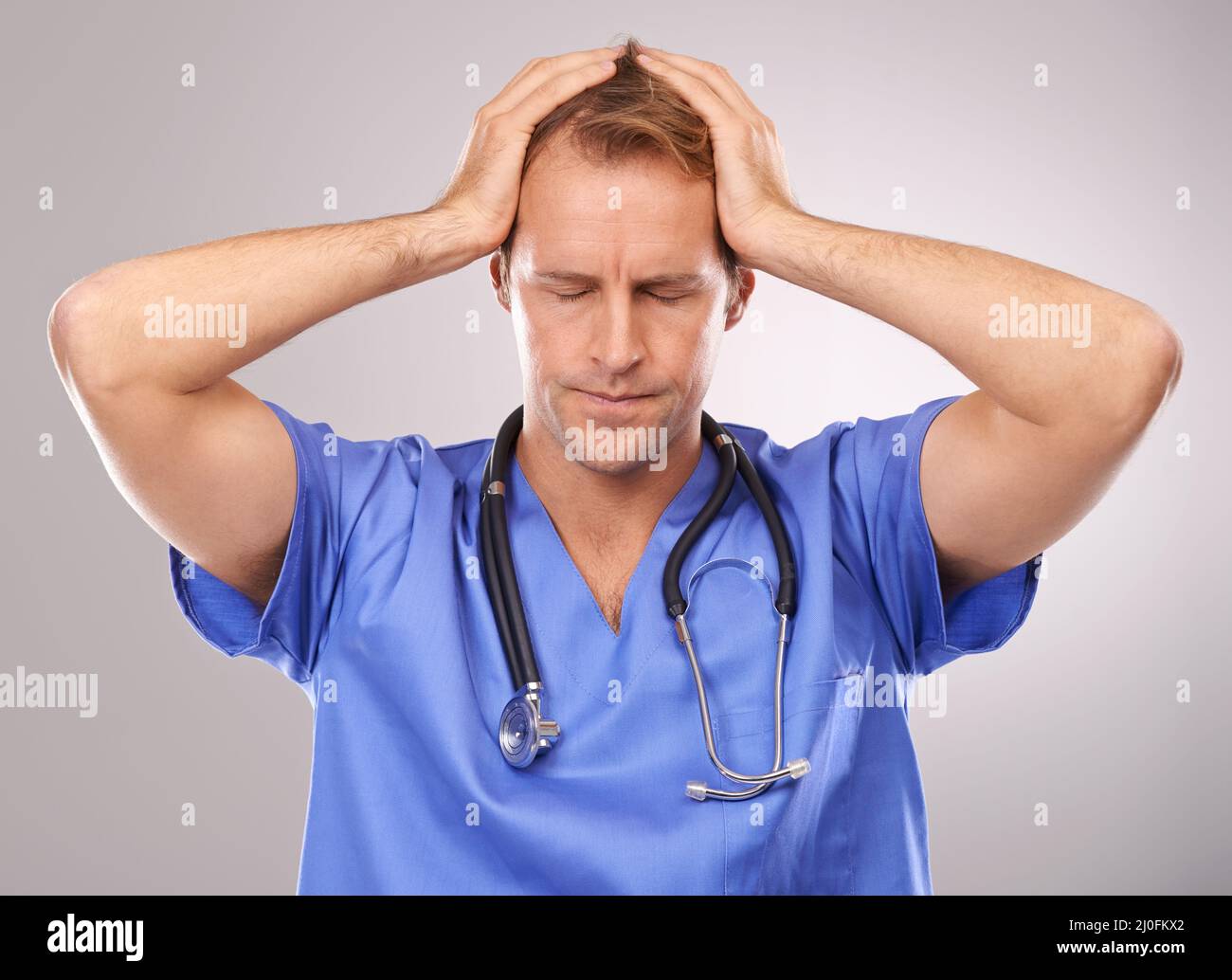 Chirurgien stressé. Studio de prise de vue d'un médecin stressé debout avec ses mains sur la tête. Banque D'Images