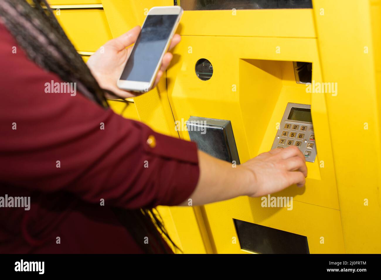 La jeune fille entre le code numérique de ramassage du colis dans la machine à colis. Clavier de communication avec une machine automatique Banque D'Images