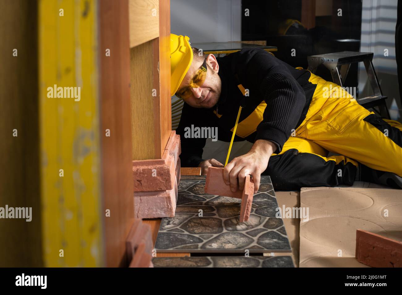 Le travailleur de la construction vérifie à l'œil si la brique décorative s'adapte à l'endroit prévu. Travailleur de la construction portant des perso Banque D'Images