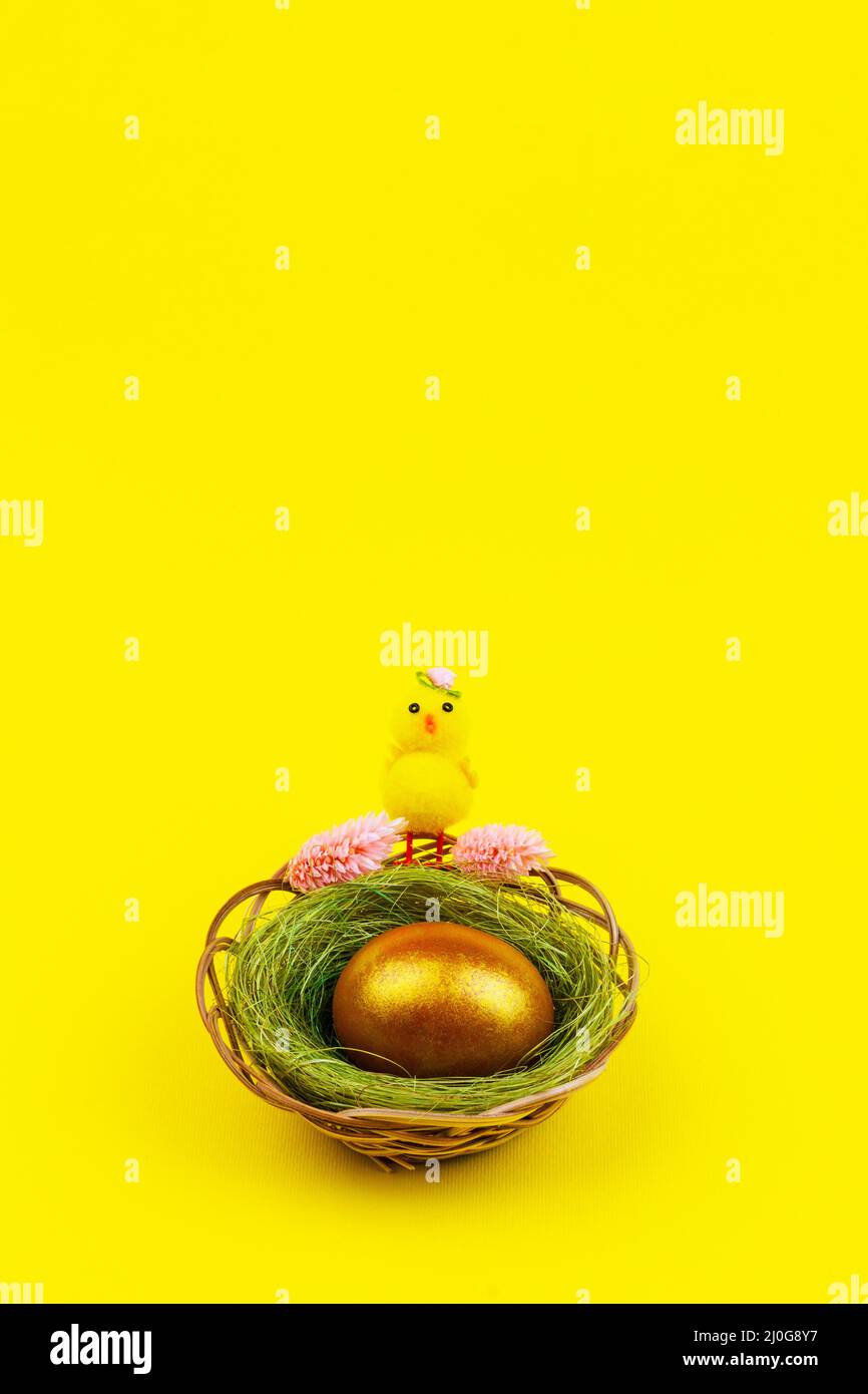 Composition de Pâques avec un poulet jaune et un œuf doré dans un nid sur fond jaune avec un espace de copie Banque D'Images