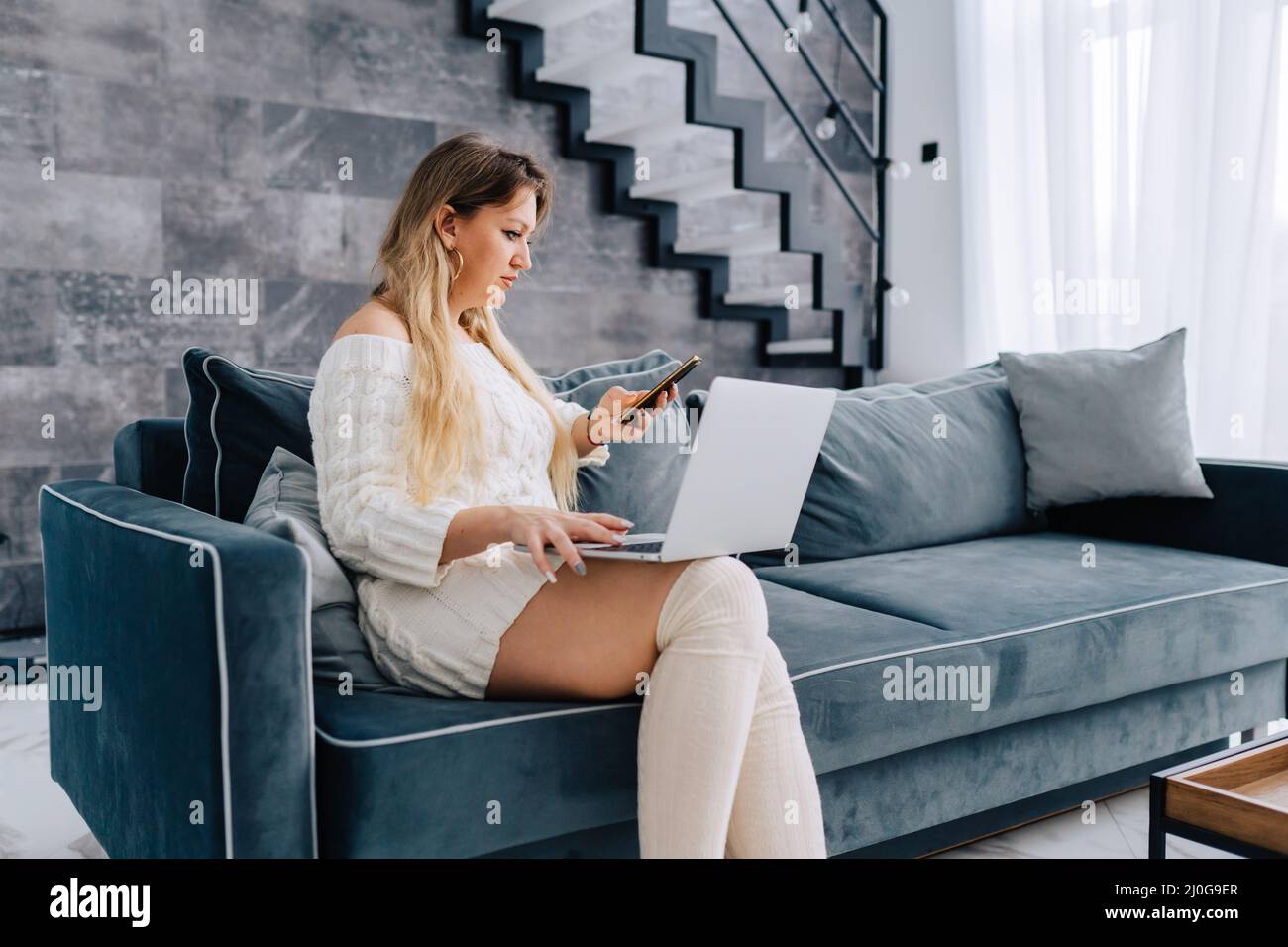 Blonde jolie femme faisant des affaires assis bleu canapé à distance travail parlant téléphone Banque D'Images