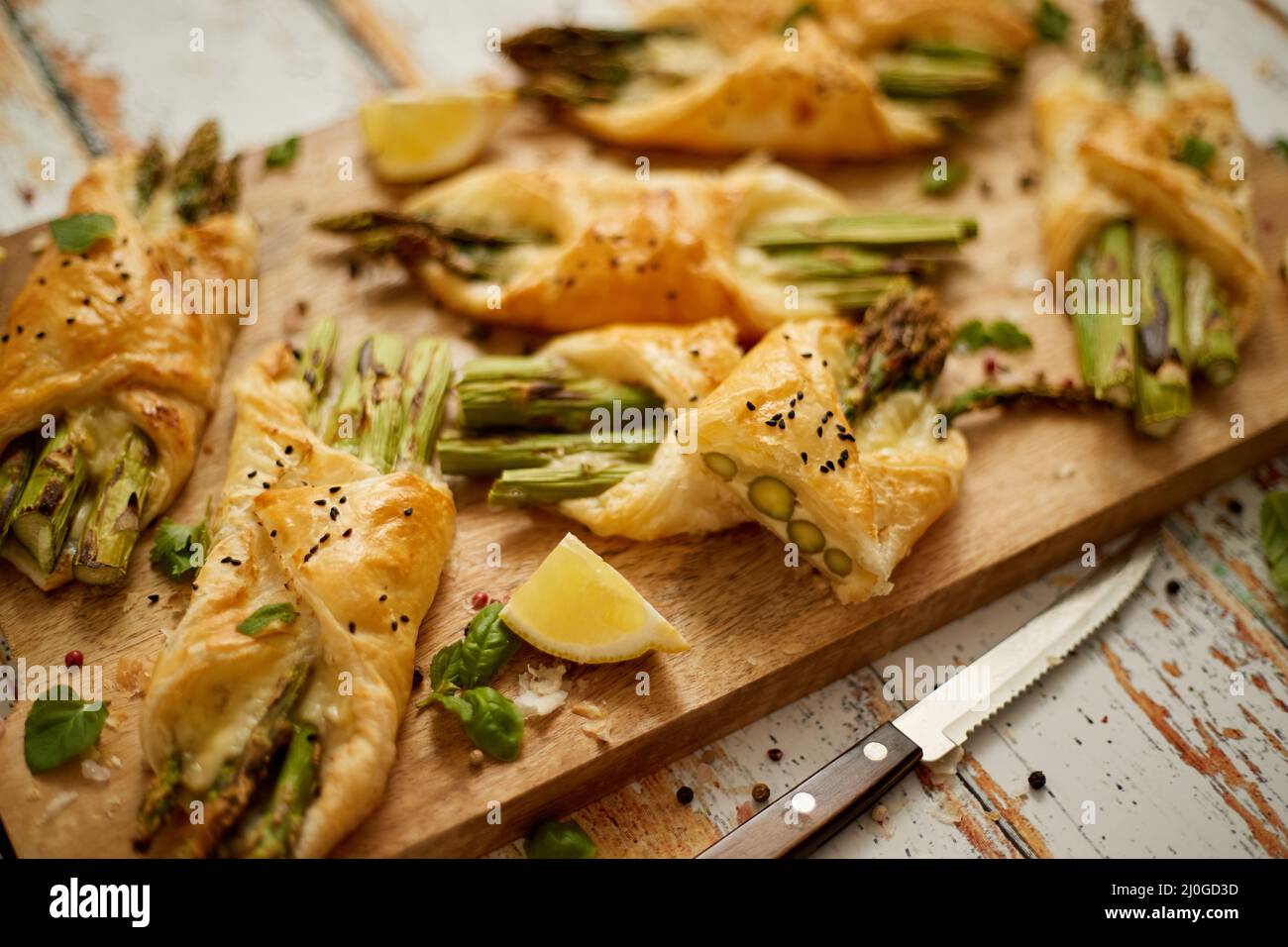 Asperges vertes cuites enveloppées de pâte feuilletée. Servi sur un panneau en bois. Avec mise au point sélective Banque D'Images