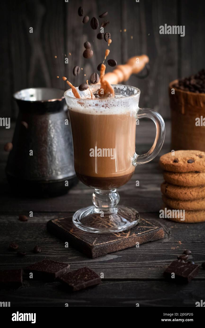 café avec crème aux éclaboussures et grains en vol avec biscuits sur fond sombre en bois Banque D'Images