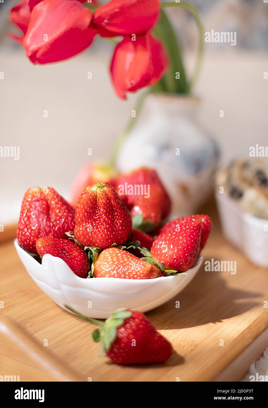 Fraises sur un plateau avec bonbons et fleurs, petit déjeuner de printemps festif. Banque D'Images