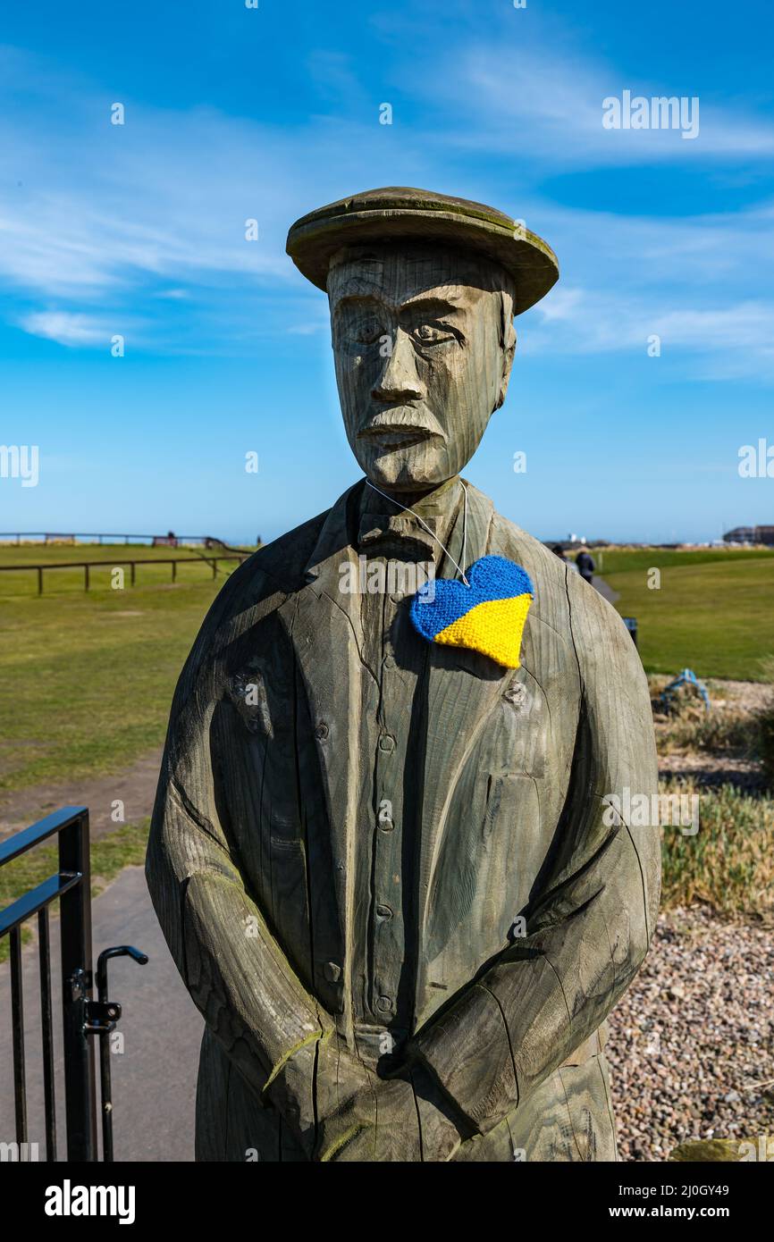 North Berwick, East Lothian, Écosse, Royaume-Uni, 19th mars 2022. Météo au Royaume-Uni : couleurs ukrainiennes. Lors d'une journée ensoleillée de printemps avec une brise raide et une température froide, North Berwick montre sa solidarité avec l'Ukraine dans différents endroits autour de la ville balnéaire. Photo : la statue en bois du célèbre golfeur de la ville, Ben Sayers, sur Elcho Green porte un coeur tricoté aux couleurs ukrainiennes Banque D'Images