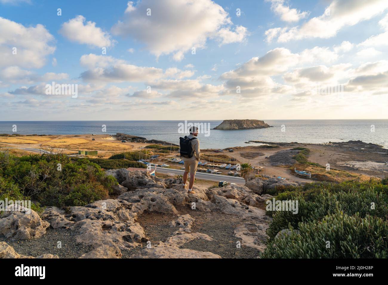 Vue sur la mer au coucher du soleil. Homme avec sac à dos sur les rochers avec belle vue sur l'île de Yeronisos près de la côte d'Agios Georgios Pegeias. Guy en Banque D'Images