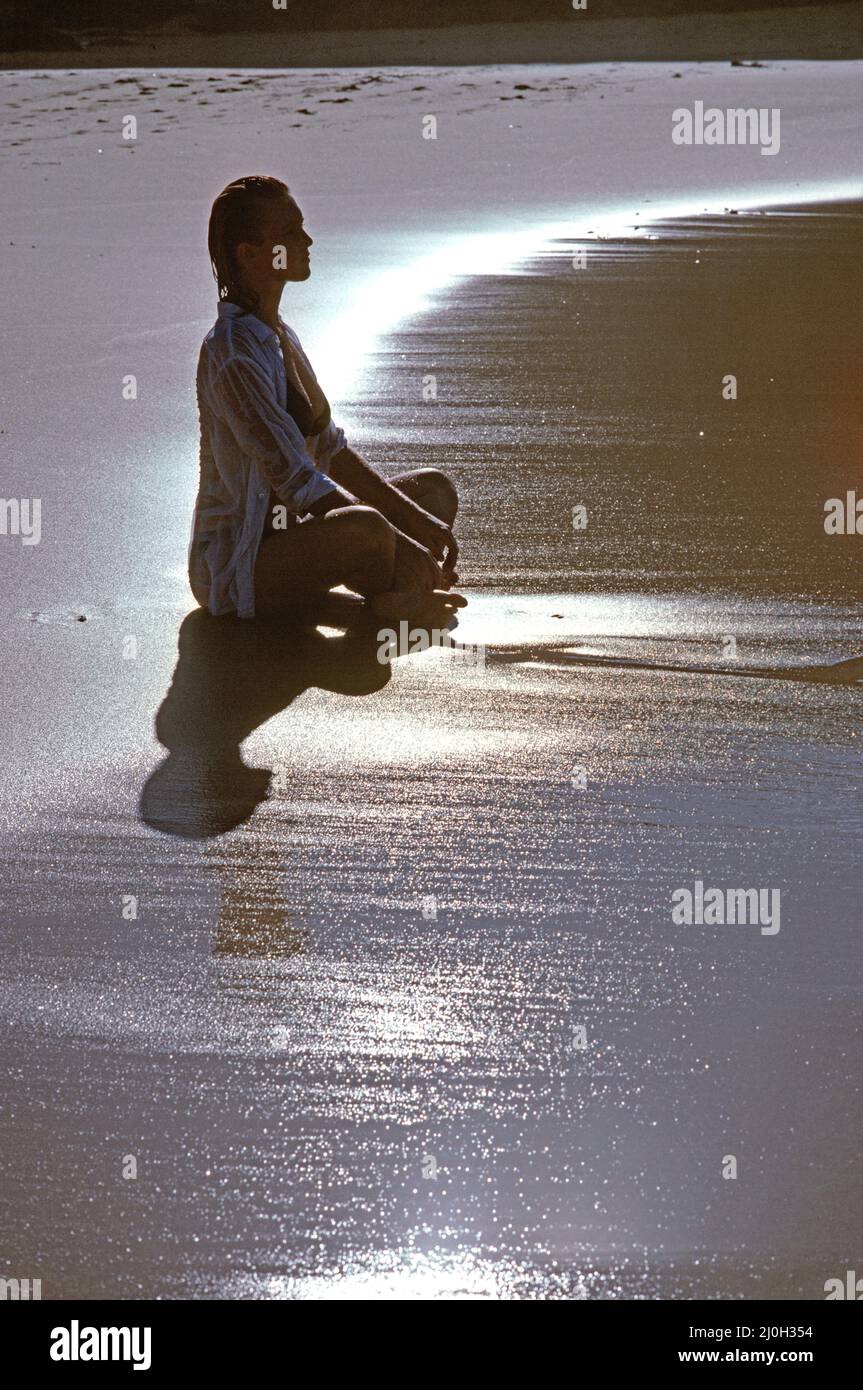 Australie. Jeune femme assise à pieds croisés sur la plage au lever du soleil. Méditer. Banque D'Images