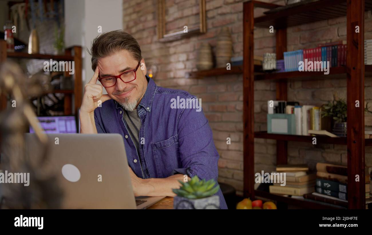 Homme d'affaires mature travaillant à domicile en ligne. Homme en 50s assis sur un bureau qui navigue sur Internet sur un ordinateur portable et le télétravail au bureau à domicile. Banque D'Images