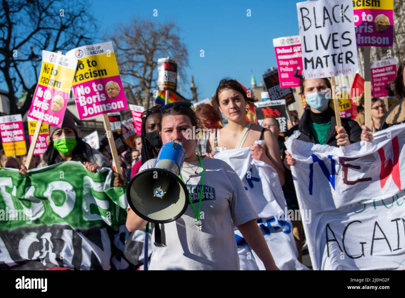 Westminster, Londres, Royaume-Uni. 19th mars 2022. Des manifestations ont lieu dans de nombreuses villes à l'occasion de la Journée des Nations Unies contre le racisme, dont l'une commence à Portland place, à Londres, avec des thèmes tels que les environnements hostiles pour les réfugiés et les migrants et le racisme institutionnel mis en évidence par les récents événements, dont l'Ukraine. La marche se dirige vers Downing Street et Parliament Square. Jeune femme blanche chantant à travers un loudhailer, dirigeant les jeunes femmes avec des plaques et des bannières Banque D'Images