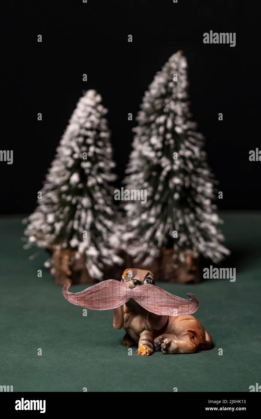 Un chien jouet avec une moustache humaine dessinée sur papier, avec des arbres enneigés en arrière-plan Banque D'Images