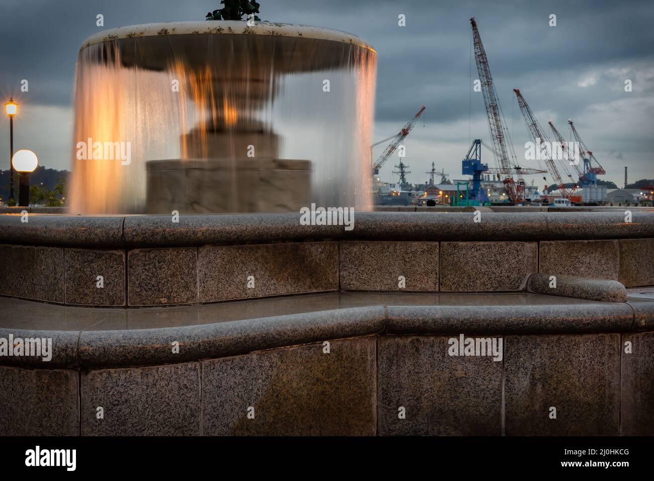 Une soirée près de la fontaine du parc Verny à Yokosuka, au Japon, avec les grues des chantiers navals de la base navale américaine en arrière-plan. Banque D'Images