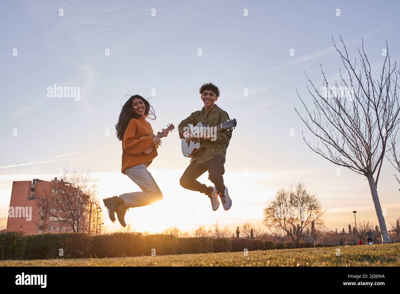 Joyeux jeune homme et jeune femme sautant avec guitare et ukulele sur ciel bleu Banque D'Images